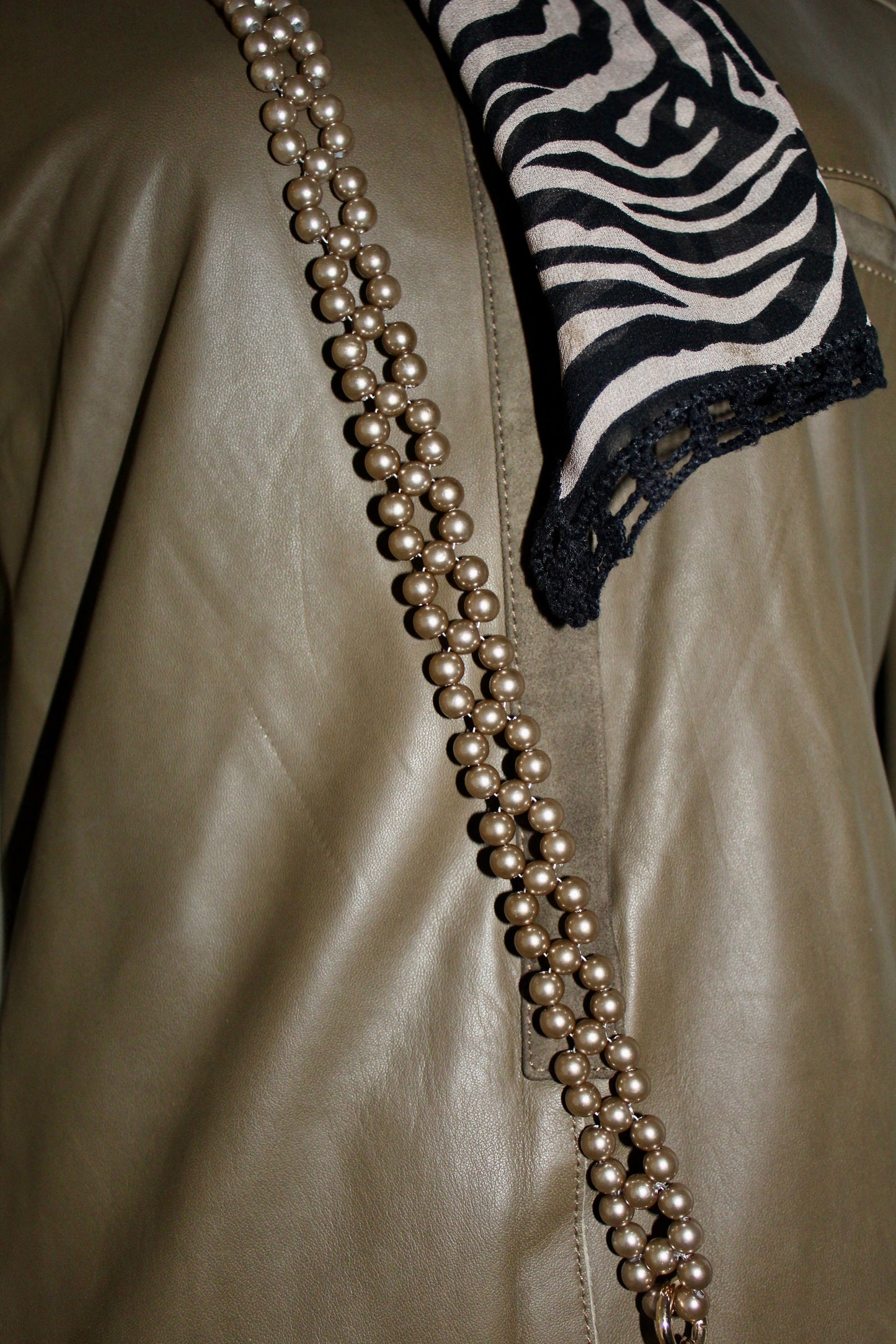 Detachable beaded chain in beige with golden rings and carabiners against a leather background.