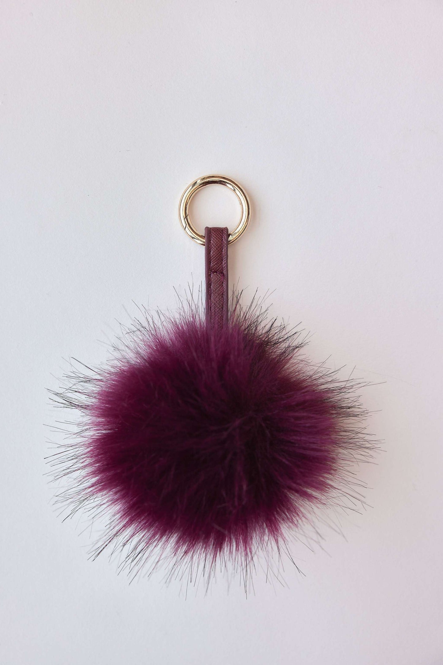 Faux fur pom-pom accessory in burgundy with gold ring for keychain or bag charm.