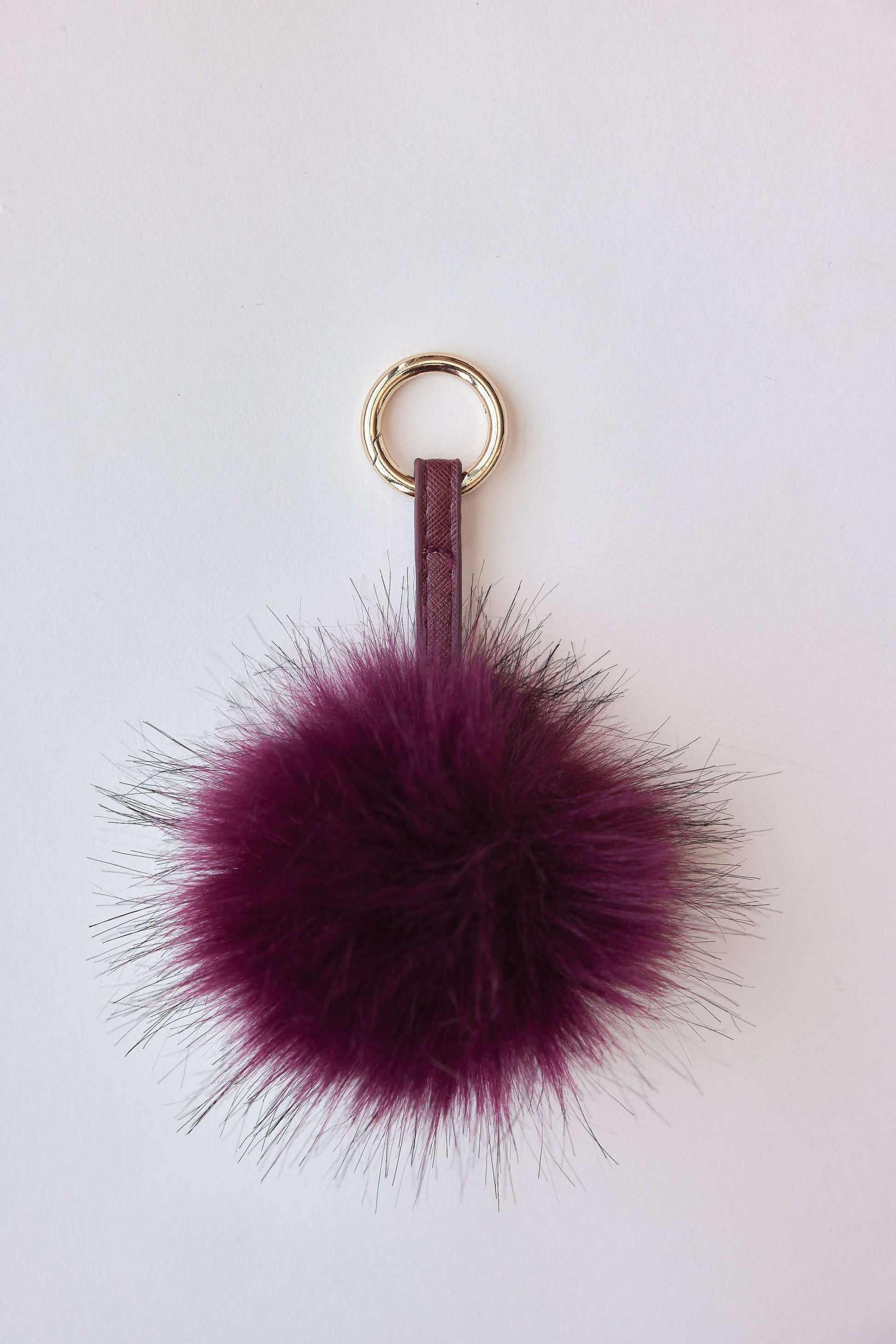 Faux fur pom-pom accessory in burgundy with gold ring for keychain or bag charm.
