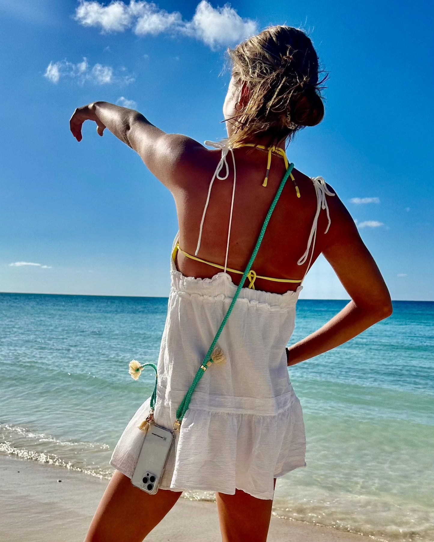Detachable cotton phone strap with double carabiners and tassel, worn by a woman at the beach.