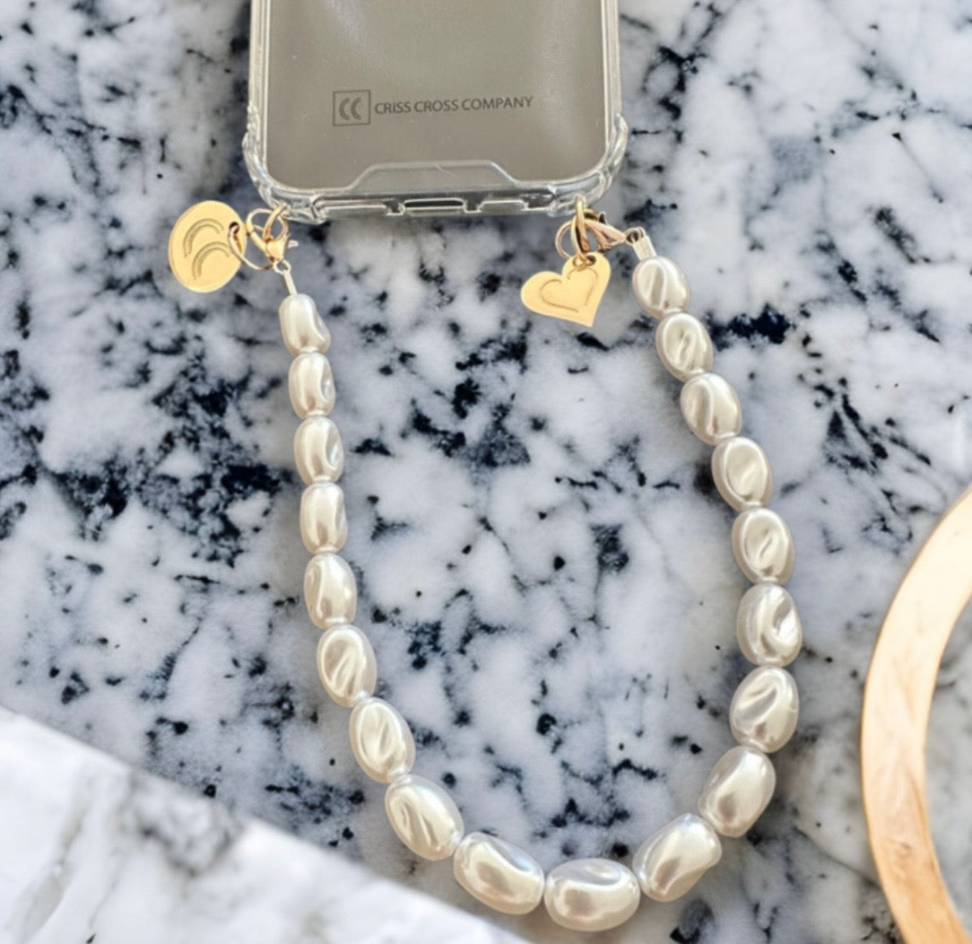 Detachable pearl wristlet attached to phone case on marble surface.