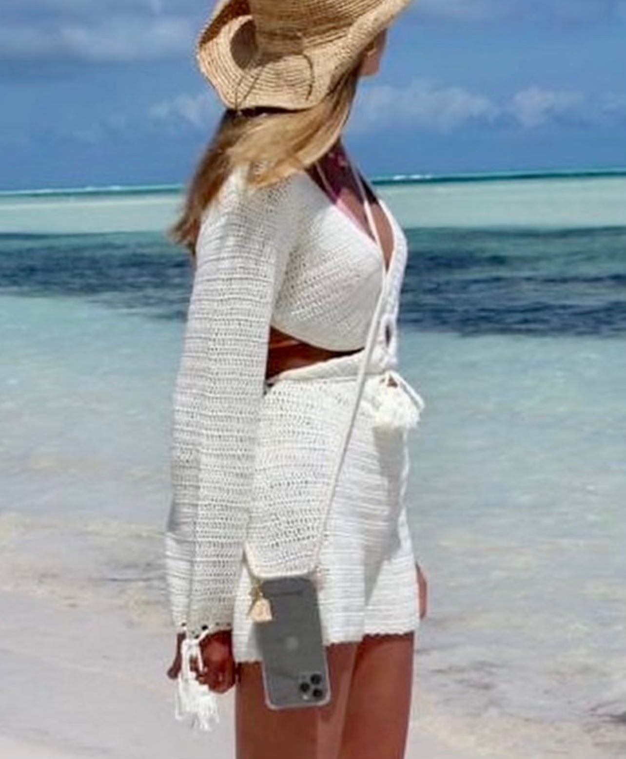 Phone case with adjustable attached cotton strap and heart charm on beach.