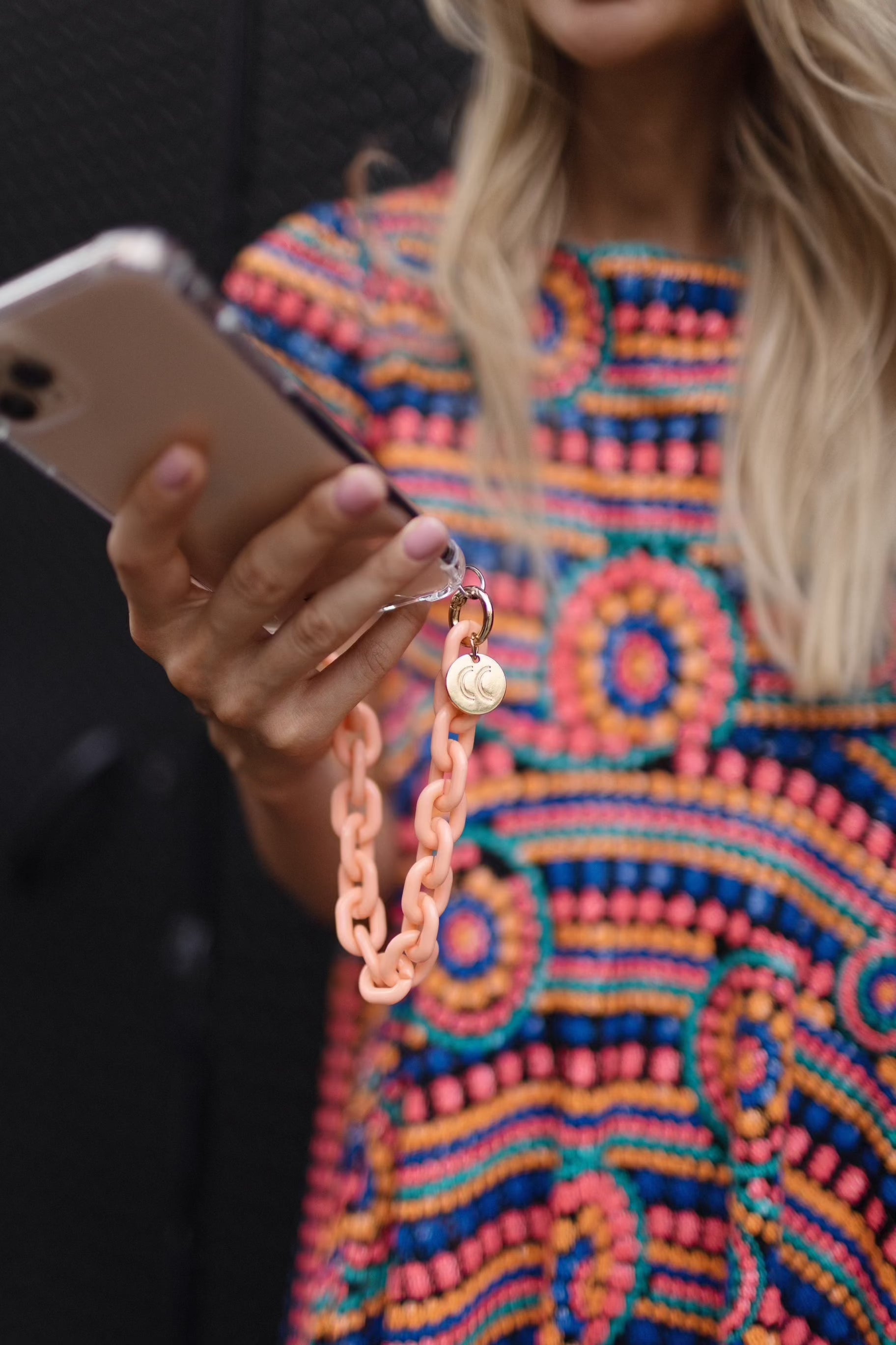 Colorful detachable phone wristlet on hand with patterned dress.