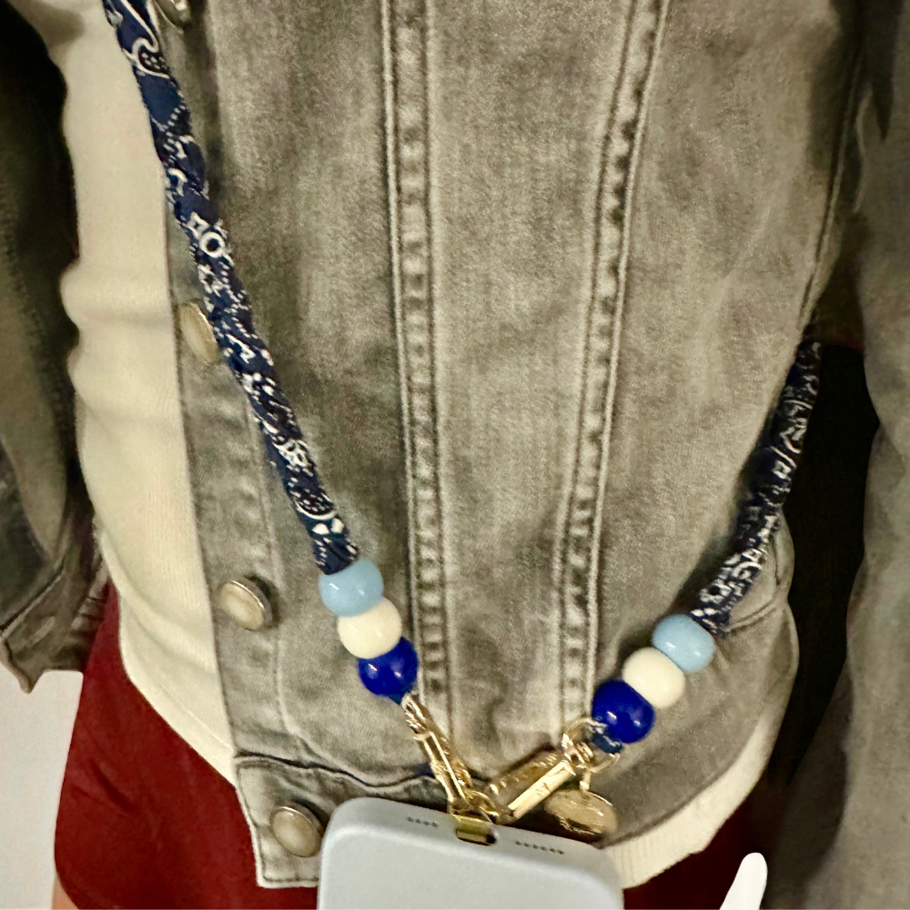 Blue bandana phone strap with beads attached to a phone case worn around the neck