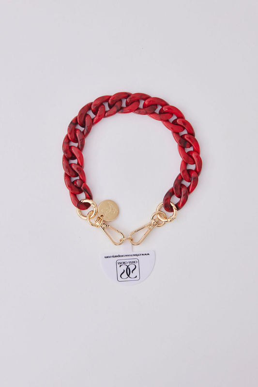 Red acrylic detachable phone wristlet with gold clasps and decorative charm on white background